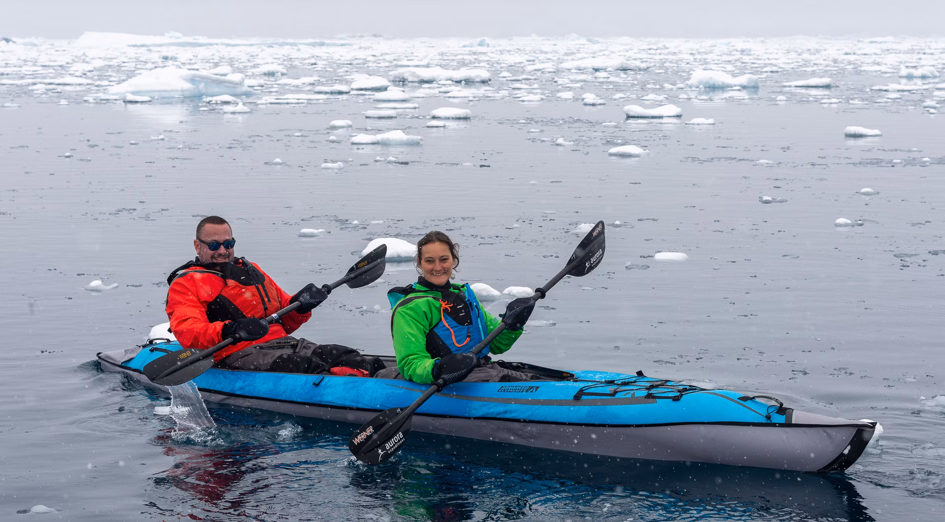 Dois hóspedes remando um caiaque duplo azul entre gelo fragmentado na Antártica